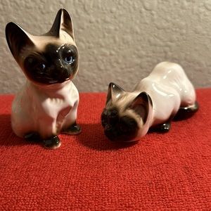 Pair of Siamese cat figurines with blue eyes. Sitting is 3” tall. Laying is 2”.
